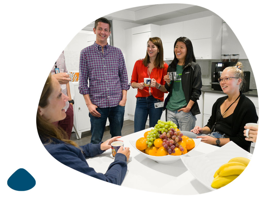 group of people talking in a room standing around a table with a fruit basket